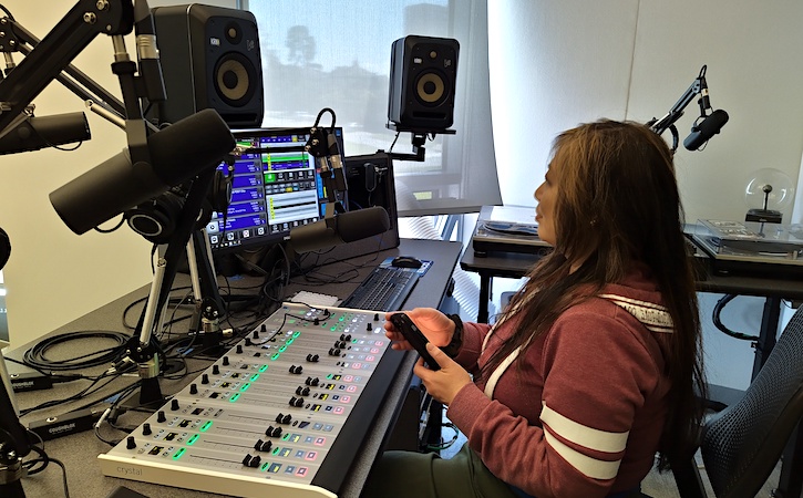 Student sitting in new studio with soundboard, computer and speakers